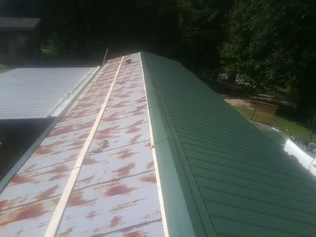 Old rusted panels beside newly installed green metal roofing — Wind Damage Roof Repair by Roofing Brothers in Grand River