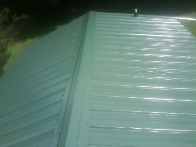 New green metal panels meeting at the ridge of a roof — Flat Roof Repair work by our crew in Grand River